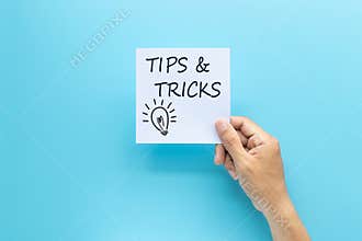 Text tips and tricks on white paper in hand isolated on blue background.