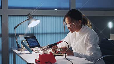 Middle close up of african american electronics engineer in protective glasses checking motherboard with multimeter