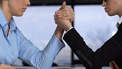 Female colleagues arm wrestling on table, career competition, business conflict