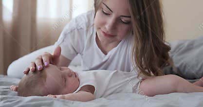 Loving mother with sleeping baby daughter on bed