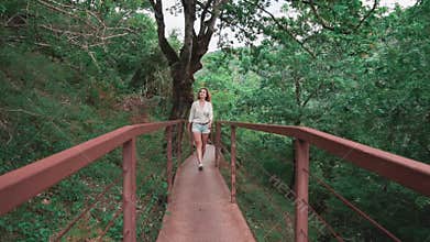 Charming slender sporty lady with gorgeous light blond hair walks along iron bridge to Okatse canyon in Georgia, amazing