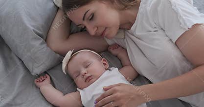 Mother with cute baby daughter sleeping on bed