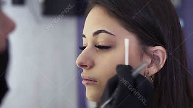 Permanent makeup. Beautiful young woman gets eyebrow correction procedure. Beautician hands in black gloves are tweezing