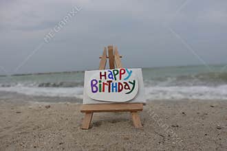 Happy Birthday message carved and painted on a stone over an easel with beach background
