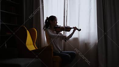 Beautiful girl musician plays on the background of a window at home