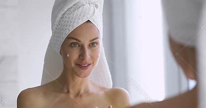 Funny woman apply skincare cream on face look in mirror