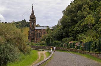 Unrecognizable tourists walking by abandoned neogothic Chapel of Nossa Senhora das Vitorias at Furnas Lake bank, Sao