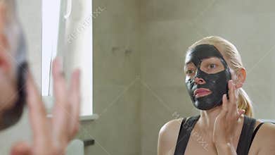 The woman puts a mud mask on a face. Face care. Mud Spa procedures. Day Spa. Drawing a black mask on the person