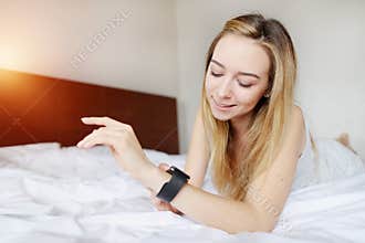 Pretty woman looking at smartwatch laying on white bed