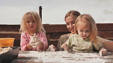Two daughters knead the dough with their hands next to their mother. Homemade bread baking.