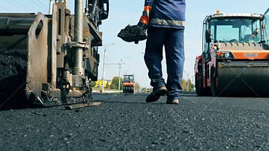 Man works on a road with machines, laying asphalt.