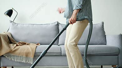 Tilt-up of happy guy in headphones dancing vacuuming carpet at home