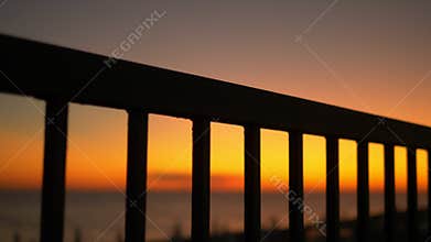 Sunset by the sea on the embankment through the bars of the fence.