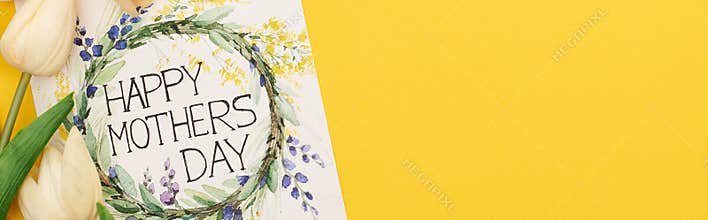 Top view of spring tulips and happy mothers day greeting card on colorful yellow background, panoramic shot