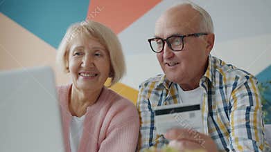 Happy elderly couple making payment online with credit card enjoying shopping