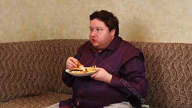 Fat man eats fast food while watching tv at home