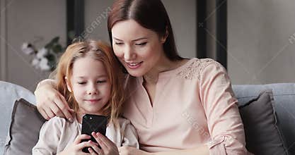 Cute kid daughter having fun with mom using smart phone