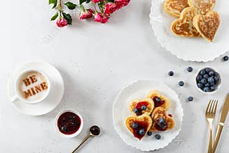 Romantic St. Valentines Day breakfast. Pancakes in heart shape, a cup of coffee with message be mine and a bouquet of roses. Cafe