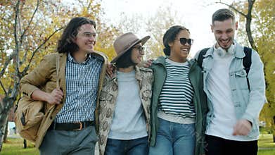 Young people multi-ethnic group walking in park with backpacks talking laughing