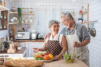 Senior couple having fun in kitchen with healthy food - Retired people cooking meal at home with man and woman preparing lunch