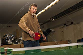 Elderly man plays table tennis at lunchtime at work.