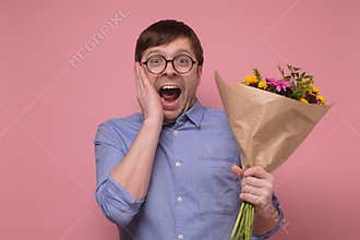 Young caucasian man in glasses having surprised face with flowers for his girlfriend