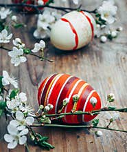 Closeup of colorful painted easter eggs and cherry blossom branch decor on vintage wooden table. Traditional seasonal holiday