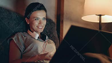 Woman starting video call on laptop. Girl waving hand to notebook camera on sofa