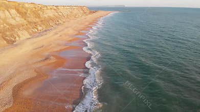 An aerial backward reveal footage of the Hengistbury Head cliff with beautiful sandy beach and crystal blue water under a majestic