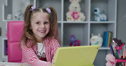 Kid girl using digital tablet technology device and looks at the camera. Small child hold tablet computer play game at