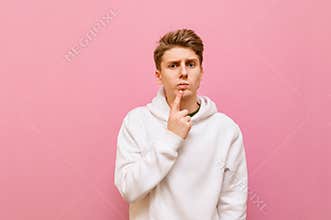 Portrait of pensive guy in casual clothing on a pink background, looks into the camera with a serious face and thinks.Student in a
