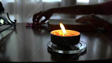 Candlelight with woman reading the holy bible at the background.