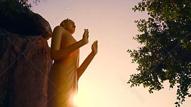 Golden statue of the standing Buddha at sunset on the monkey mountain in Hua hin. Standing Buddha in the sun rays of the sunset.