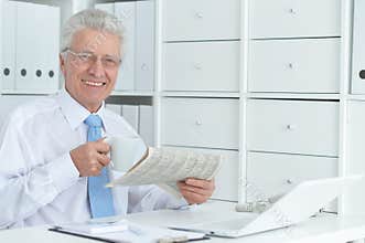 Beautiful old caucasian man with laptop reading newspaper