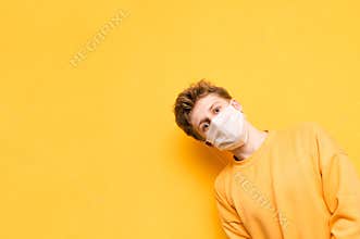 Funny guy in bright casual clothes and medical mask on his face looks from the right side with smile on his face and looks at the