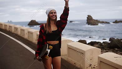 Front view of sporty builded woman in hat, coat and short shorts enjoying time by the seaside on a cloudy day at sunset