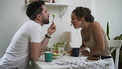 Bearded man and beautiful woman are eating dinner and kissing at table in home kitchen spbd.