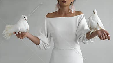 Portrait of a young newlywed young bride in a beautiful white dress with a cleavage, holding two white doves in her hands,