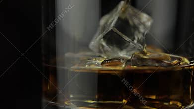 Pouring alcohol drink whiskey, cognac into glass with ice cubes. Slow motion
