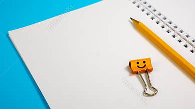 Blank Paper Notepad with Orange Color Pencils and Smile Binder Clip on Blue Background