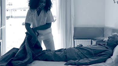 Nurse helping elderly man going into hospital bed. Sepia toned