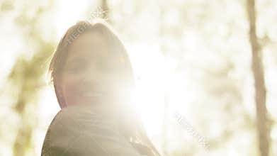 Portrait of happy teenage girl with toothy smile playing with hair. Sun ray coming throught the tree branches