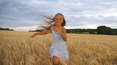 Beautiful happy girl with long blonde hair running to the camera through wheat field. Little smiling kid jogging over