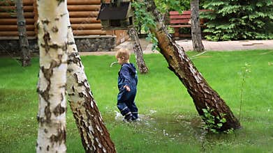 Little cute playful caucasian blond toddler boy enjoy have fun playing jumping in dirty puddle wearing blue waterproof
