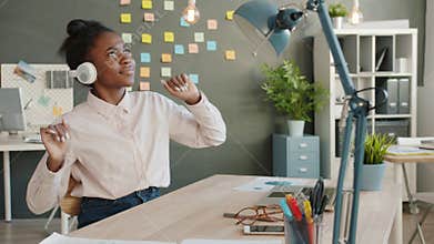African American office worker relaxing at work listening to music and dancing at desk with laptop