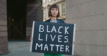 Portrait of young woman with nose ring holding carton placard with black lives matter writing. Millennial girl