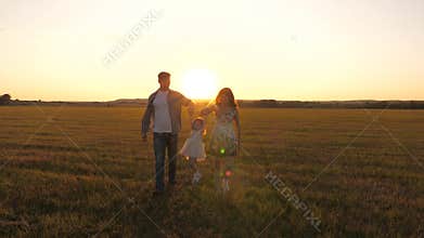 Little daughter holds mom and dad by hands and jumps on meadow in park in rays of yellow sun. Family happiness. healthy