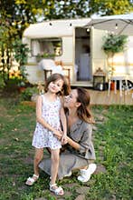 Young woman hugging cute daughter near house on wheels.