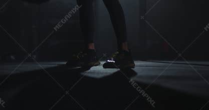 In front of the camera athletic guy details using a cross fit ball doing hard exercises for his muscle in a dark gym
