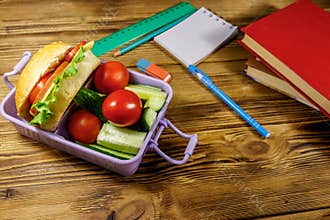 Back to school concept. School supplies, books and lunch box with burgers and fresh vegetables on wooden table
